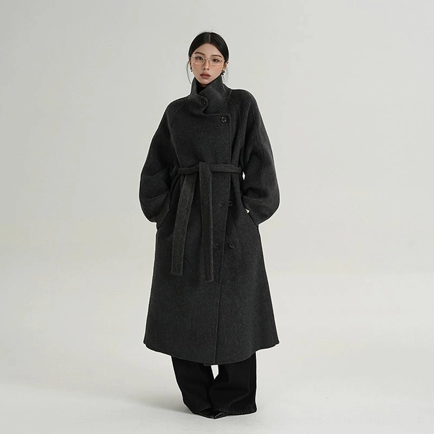 Three-quarter view of a woman wearing a belted dark gray wool cocoon coat with stand collar, double-breasted buttons, and relaxed longline fit
