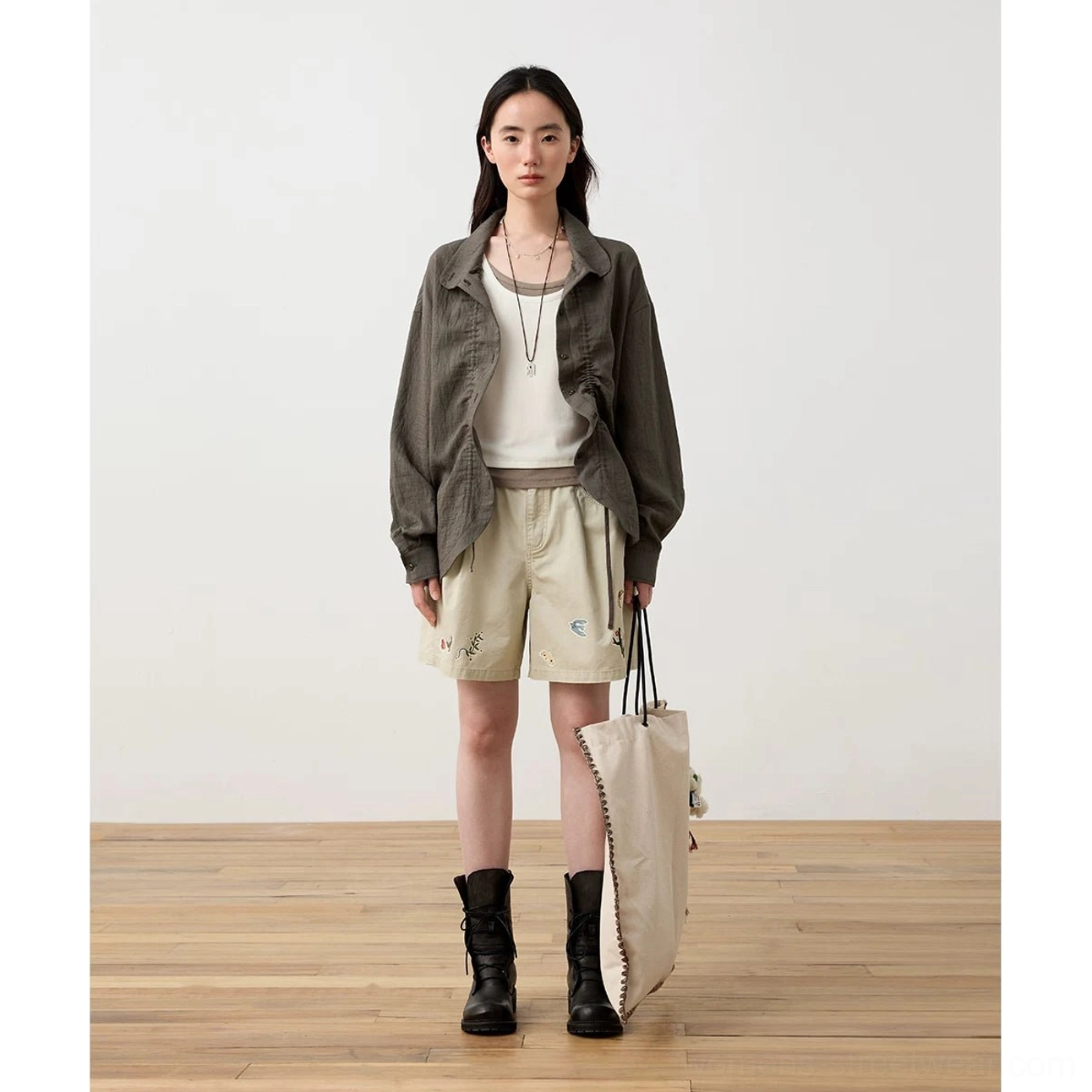 Dark gray crinkled textured long-sleeve Mandarin collar shirt styled with a white camisole, embroidered shorts, combat boots, and canvas tote