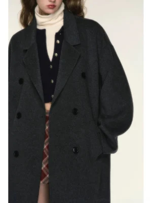 Close-up detail of dark charcoal gray double-breasted wool coat showing structured notch lapels, round buttons, soft fuzzy merino texture, and vertical welt pocket