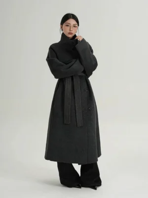 Dark gray oversized funnel neck wool coat styled with a detachable waist belt, buttoned front, long sleeves, and black wide-leg pants