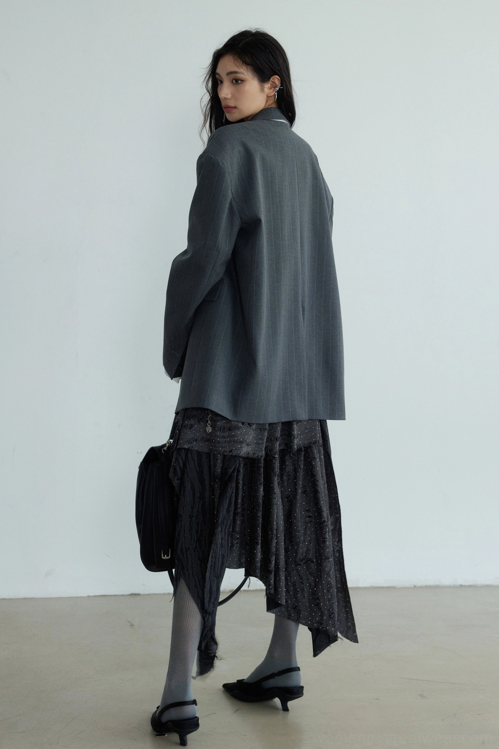 Side back view of a dark gray genderless striped blazer showing the loose silhouette fabric drape and crossbody bag styling