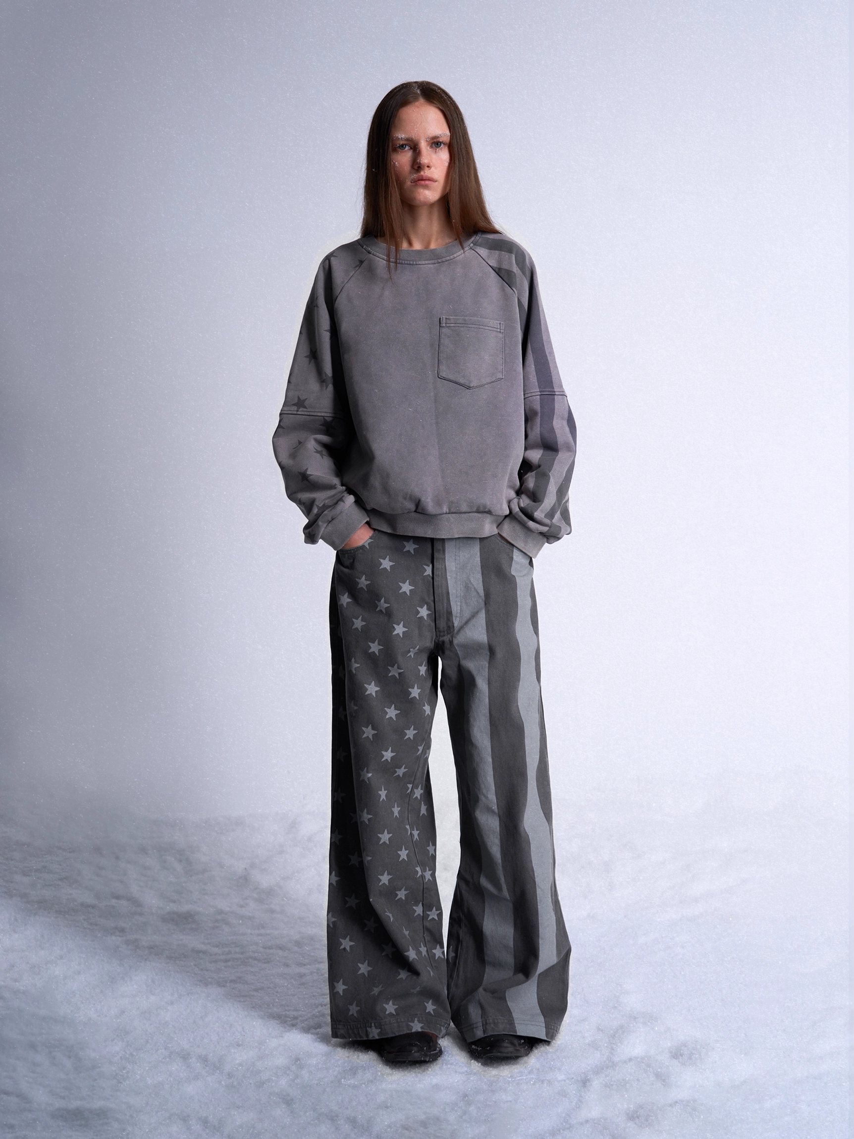 Full body front view of dark gray graphic wide leg jeans styled with a coordinated gray crewneck sweatshirt