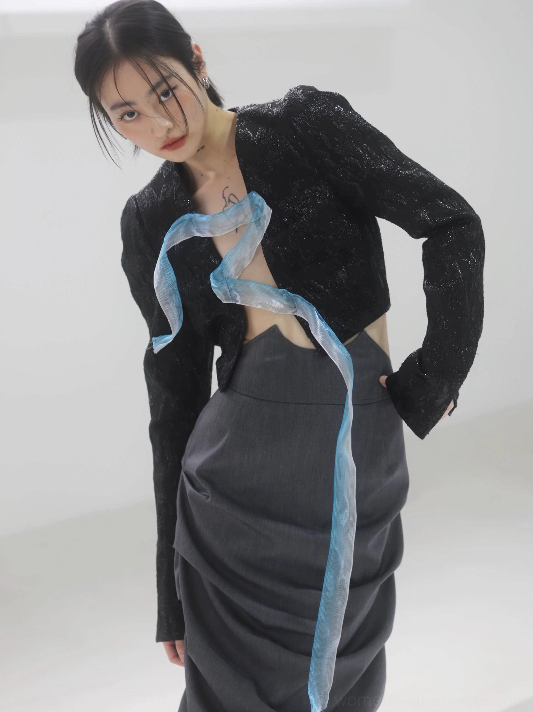 Medium close-up of a dark gray high-waisted ruched midi skirt showing the sculptural gathered texture beside a cropped black top with a blue sheer ribbon detail