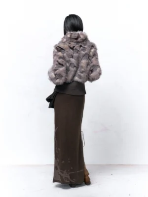 Back view of a dark gray knitted maxi skirt with subtle abstract splash pattern, side drawstring detail, and brown ankle boots styled with a cropped faux fur jacket