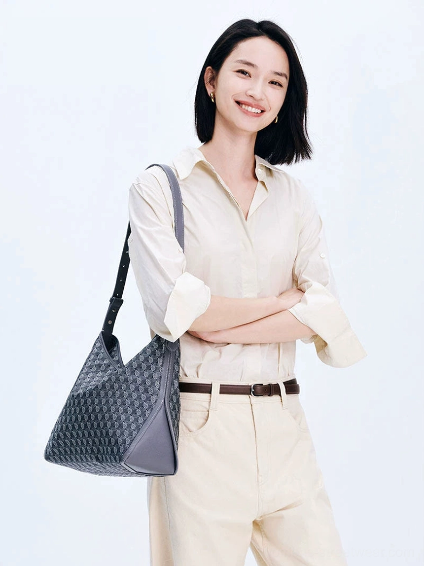 Model wearing dark gray monogram large hobo shoulder bag with minimalist beige office casual outfit