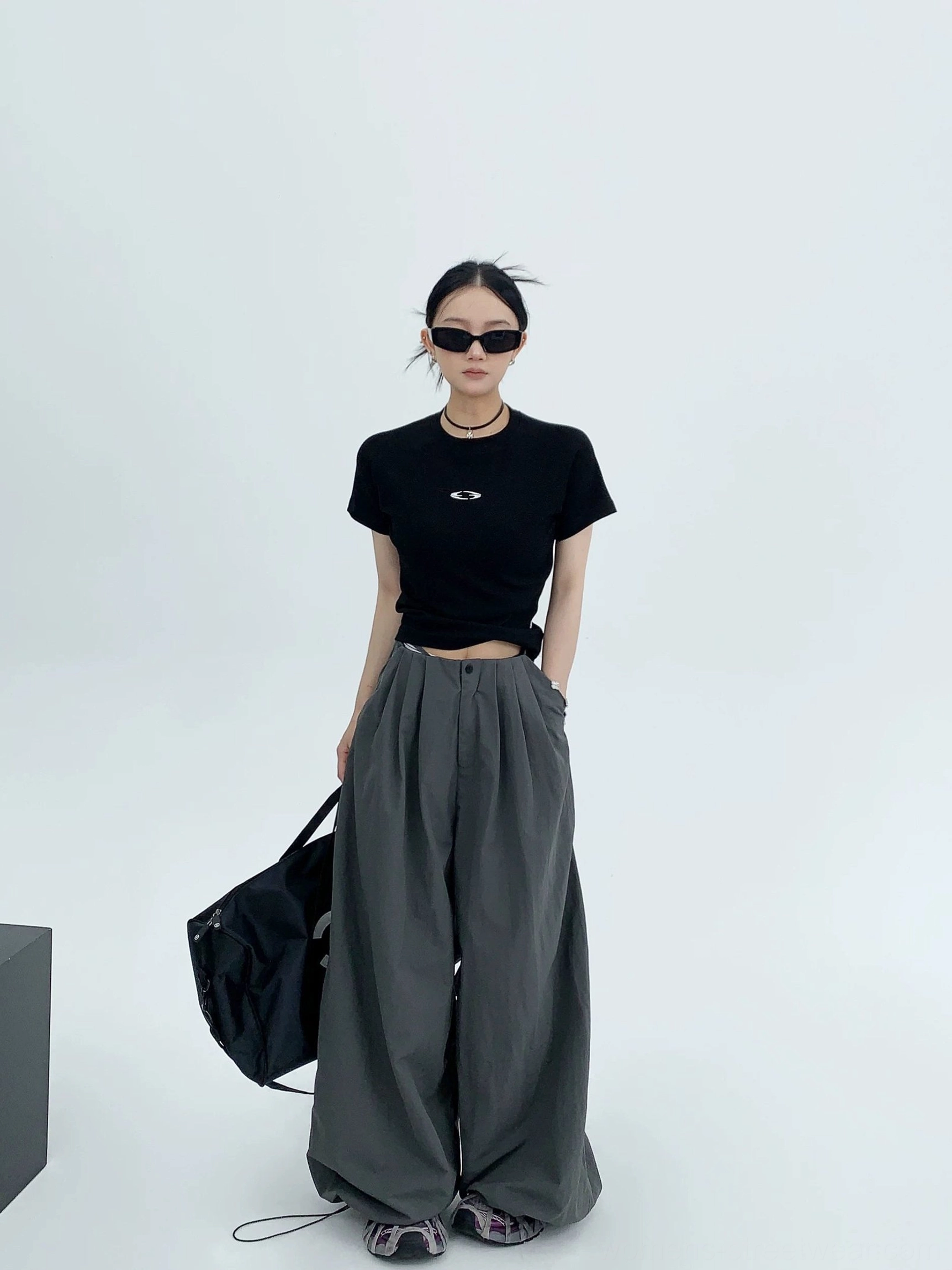 Dark gray oversized streetwear pants with pleated drawstring waist styled with a cropped black tee and large tote bag