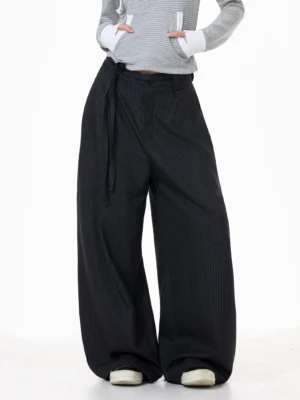 Front three-quarter view of dark gray pinstripe wide-leg streetwear trousers styled with a cropped hoodie and off-white sneakers