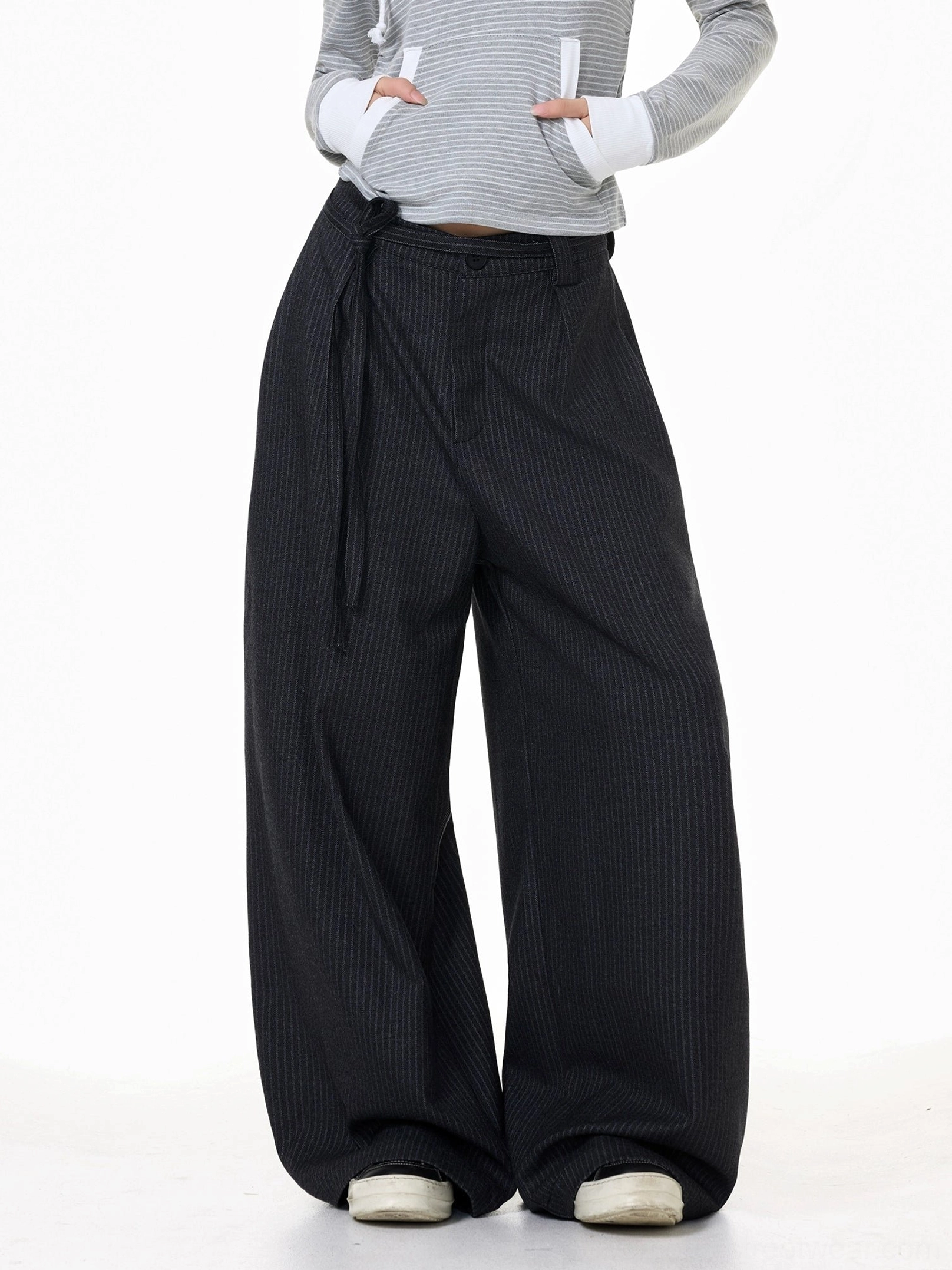 Front three-quarter view of dark gray pinstripe wide-leg streetwear trousers styled with a cropped hoodie and off-white sneakers