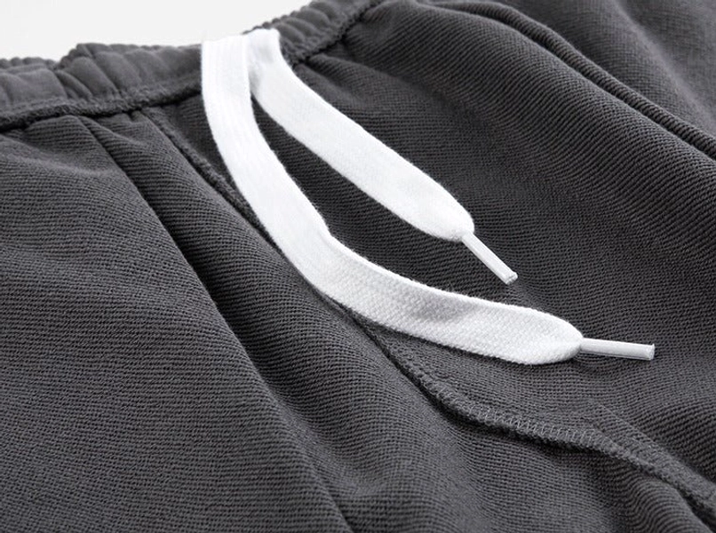 Close-up of white cotton drawstrings, tipped ends and front waist pleats on dark gray relaxed fit streetwear shorts