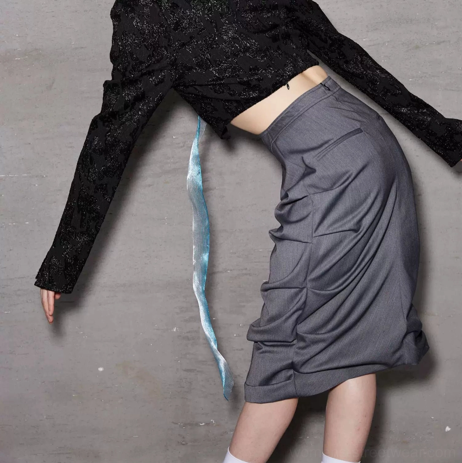 Flat detail view of a dark gray ruched midi skirt showing the asymmetric draped construction and gathered texture on a concrete gray background