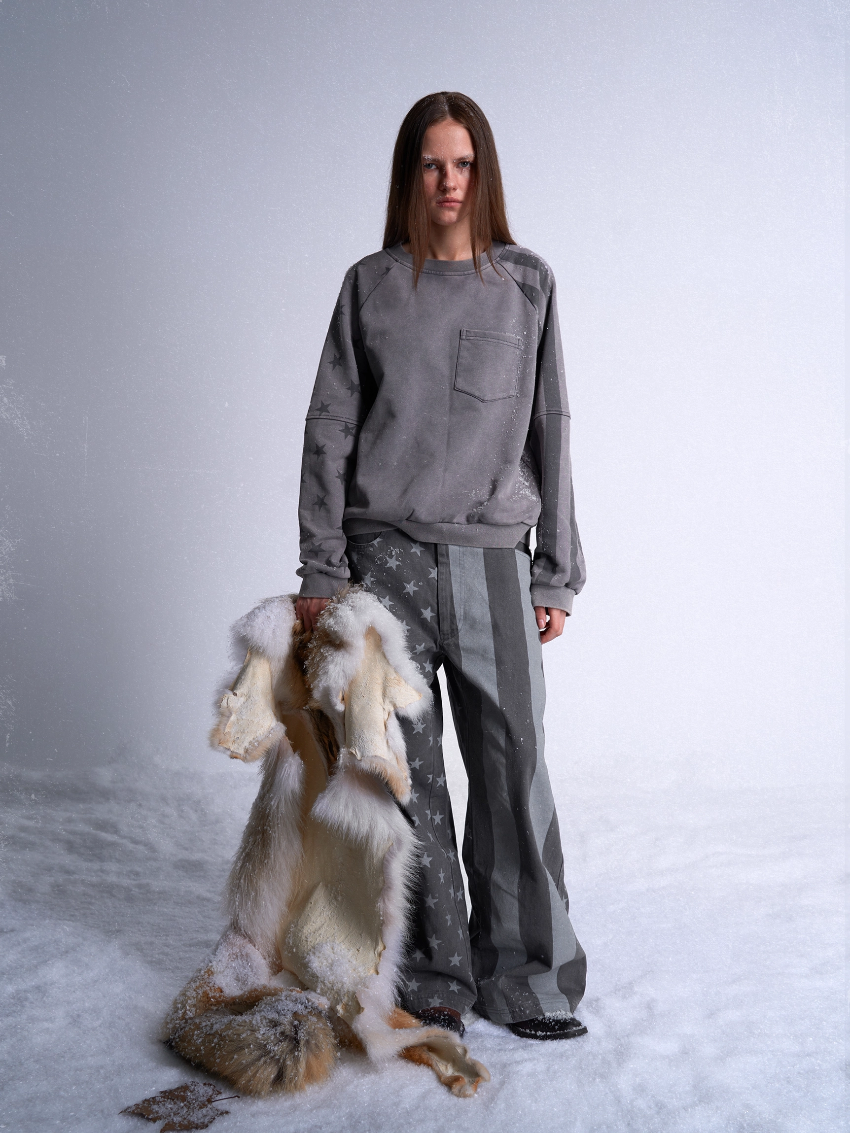 Full body front view of dark gray stars and stripes wide leg streetwear jeans styled with a matching gray sweatshirt