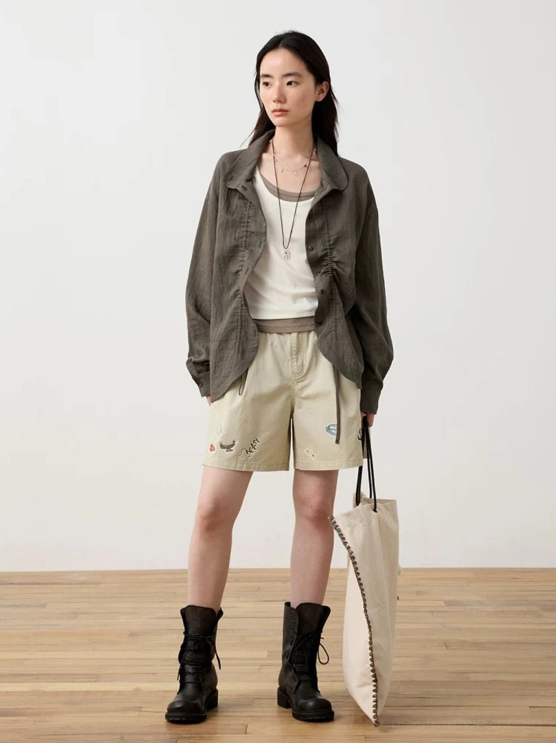 Dark gray textured relaxed button shirt worn over a white camisole with embroidered beige shorts, combat boots, and canvas tote bag
