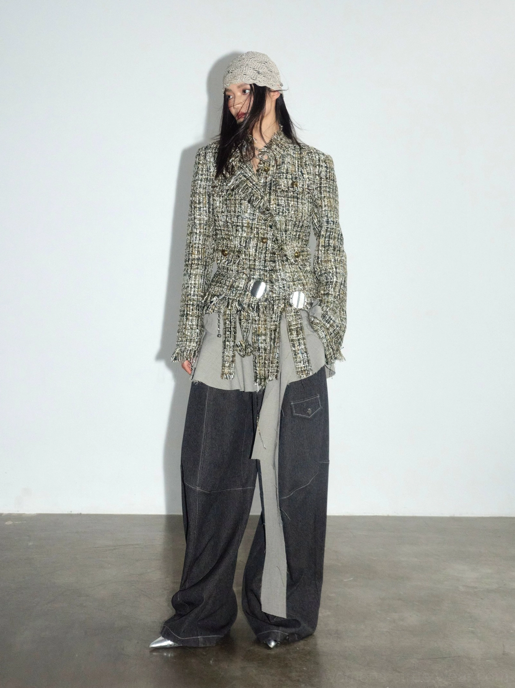 Dark gray wide leg cargo trousers paired with a tweed jacket, metallic waist belt, contrast layered hem, and beanie in a modern urban outfit