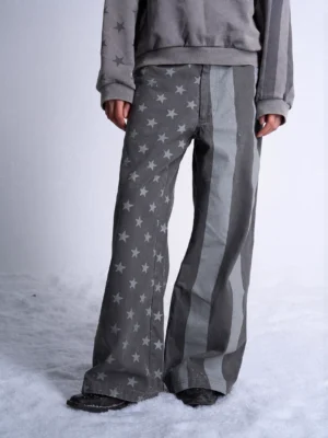 Close front view of dark gray wide leg jeans showing light gray star print on one leg and vertical stripe panels on the other
