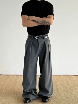 Dark gray wide-leg pleated trousers styled with a black crewneck T-shirt and dress shoes, highlighting the tailored waistband, smooth suiting finish, and relaxed streetwear silhouette