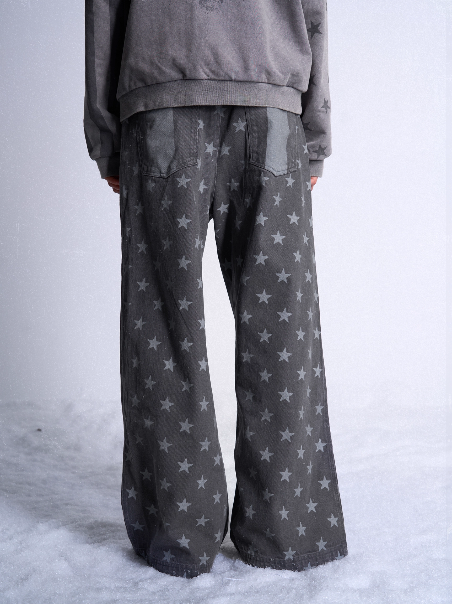 Rear view of dark gray wide leg streetwear jeans with all-over light gray star graphics and classic back pockets