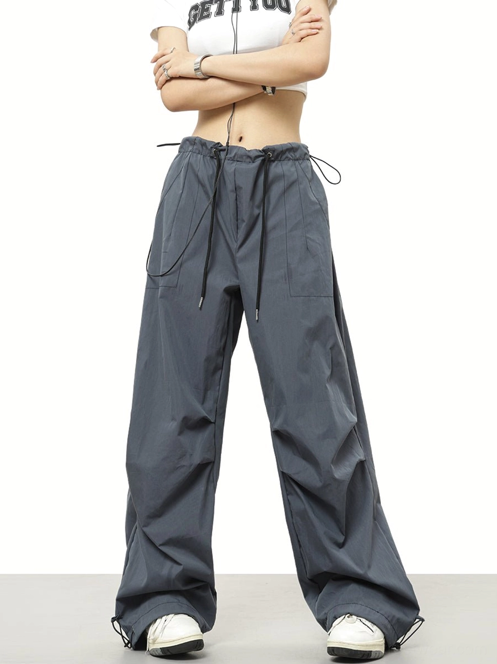 Dark gray wide-leg streetwear pants with side utility pockets, drawstring waist, and adjustable cuffs styled with a white graphic tee