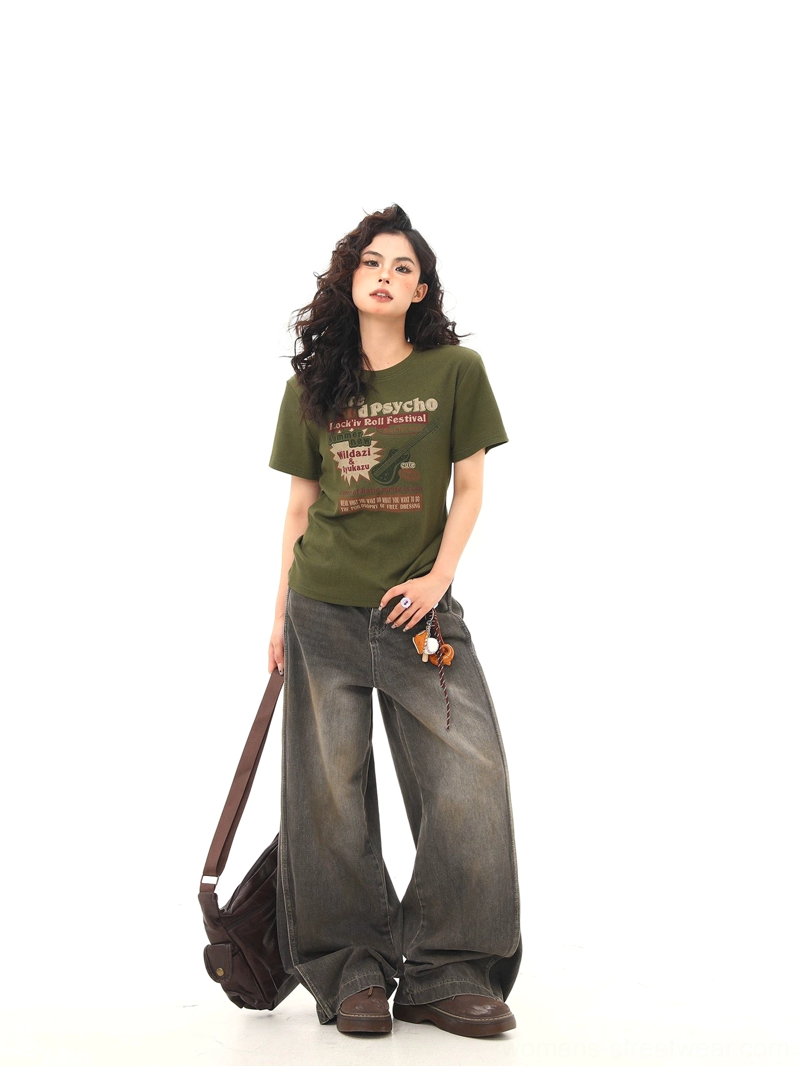 Full front view of a dark green vintage festival T-shirt with chest guitar graphic, styled with wide-leg denim and a brown crossbody bag