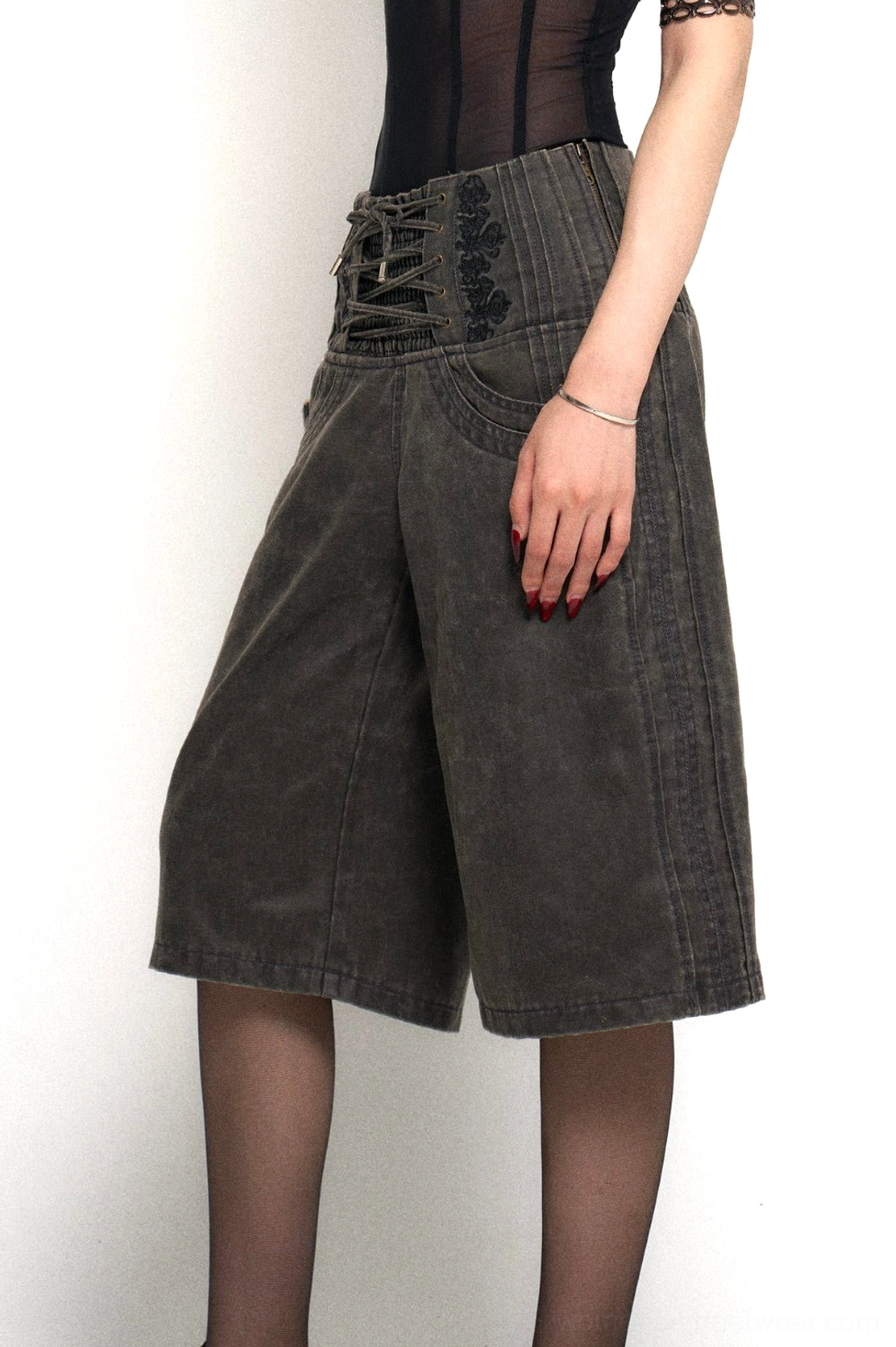 Close-up of dark grey distressed denim culotte pants featuring decorative high-waist lace-up detailing, front pockets, and wide-leg streetwear construction