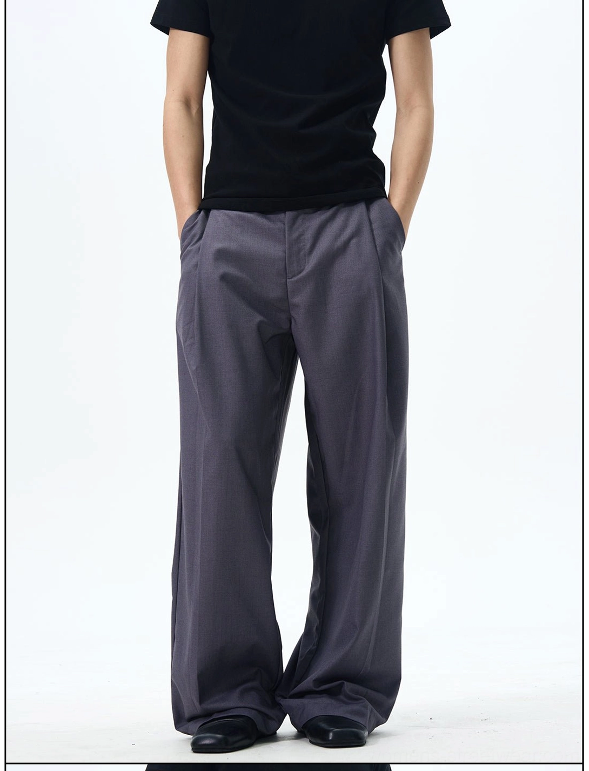 Close-up of dark grey high-waisted pleated streetwear dress pants showing front pleats, waistband, and side pockets