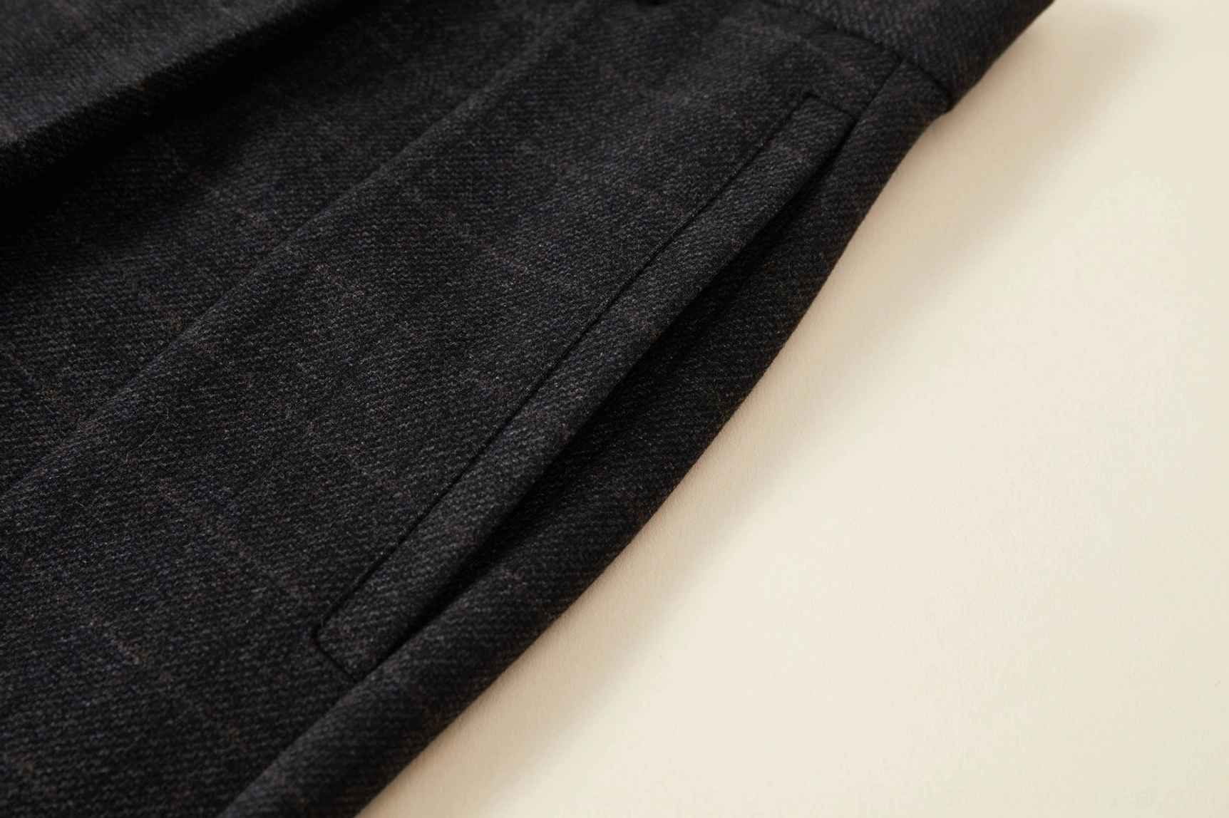 Close-up view of the hidden side seam pocket and textured suiting fabric on dark grey plaid streetwear trousers