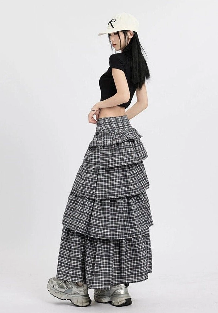 Side back view of a dark grey plaid tiered maxi skirt with a flowing full length cake skirt silhouette and streetwear outfit