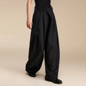 Three-quarter view of dark grey plaid wide-leg streetwear trousers with front pleats, tailored waistband, black top, and leather loafers