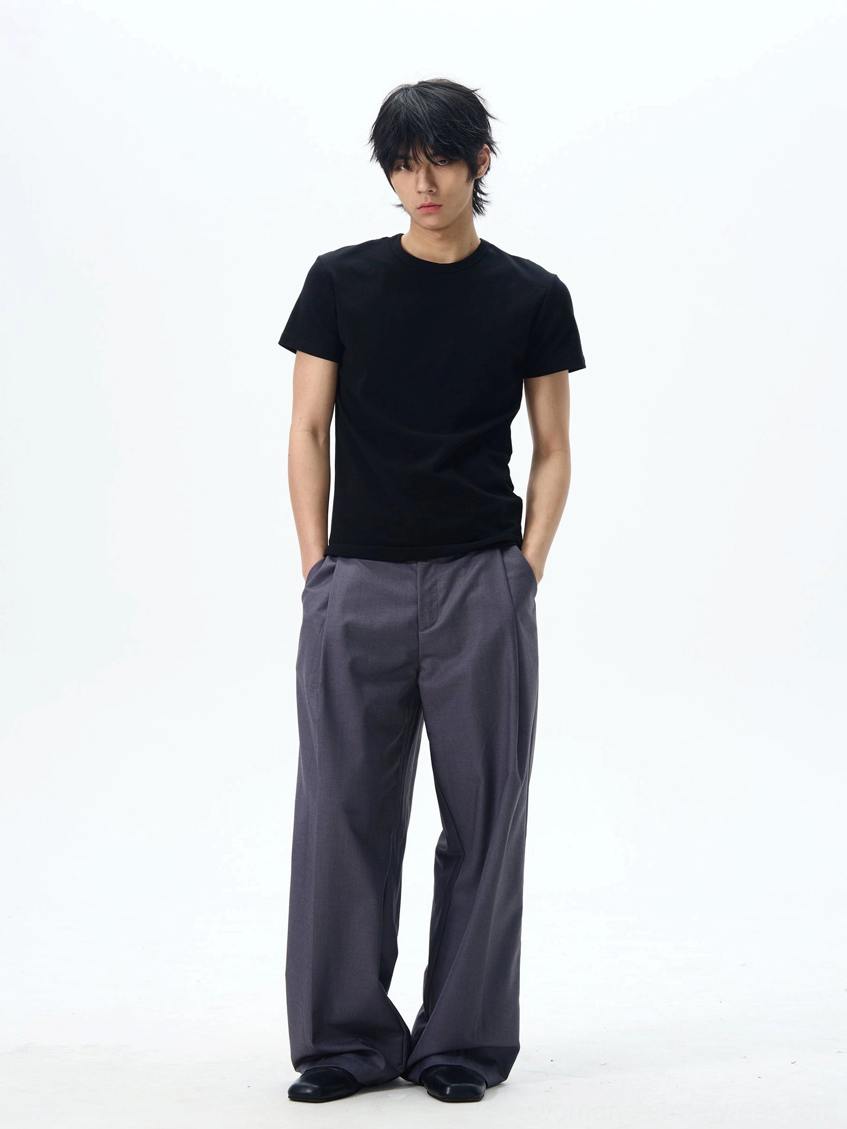 Dark grey pleated wide-leg dress pants shown on a male model in a relaxed Korean streetwear outfit with side pockets