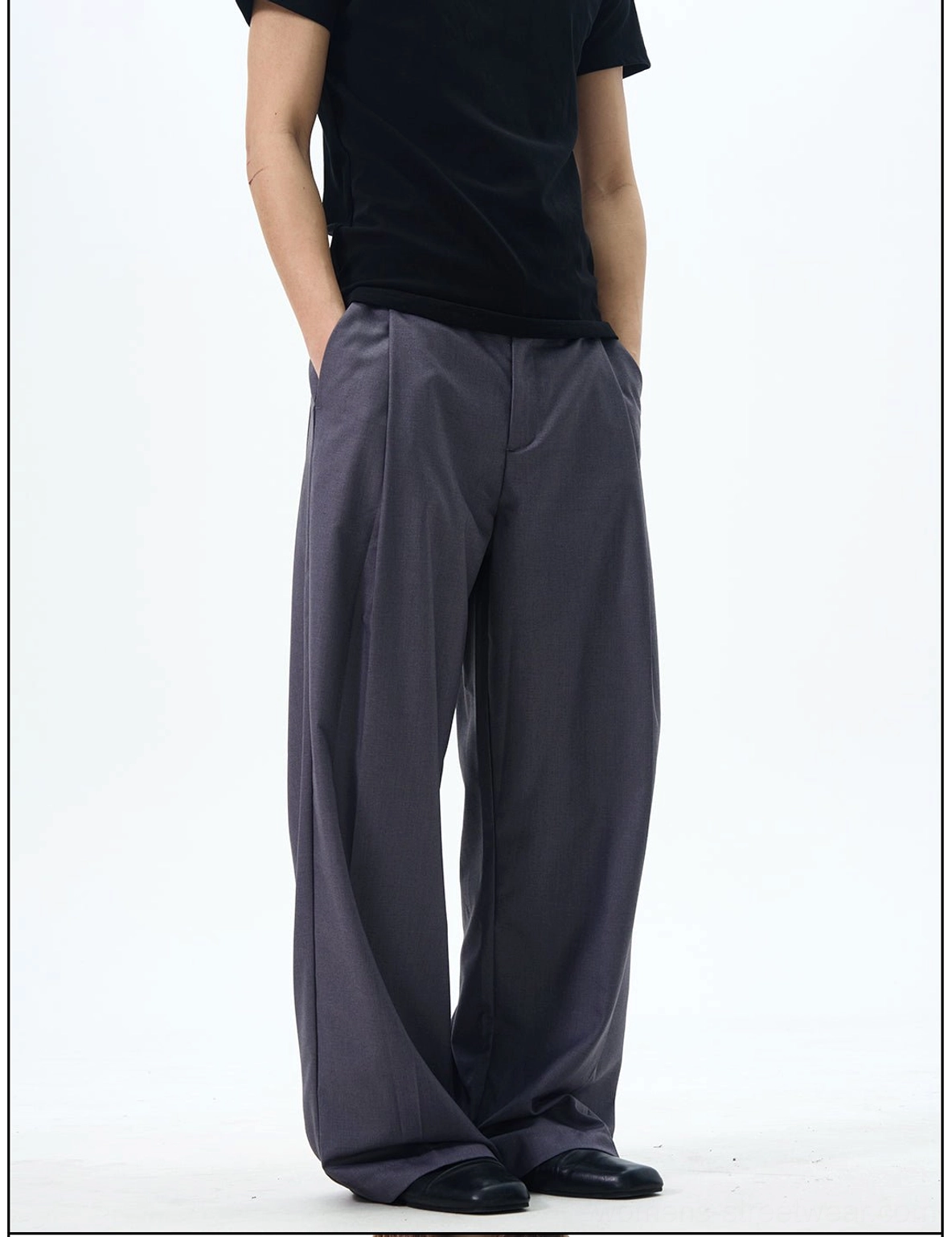 Side close-up of dark grey pleated wide-leg trousers showing the tailored waistband, structured pleats, and fluid trouser drape