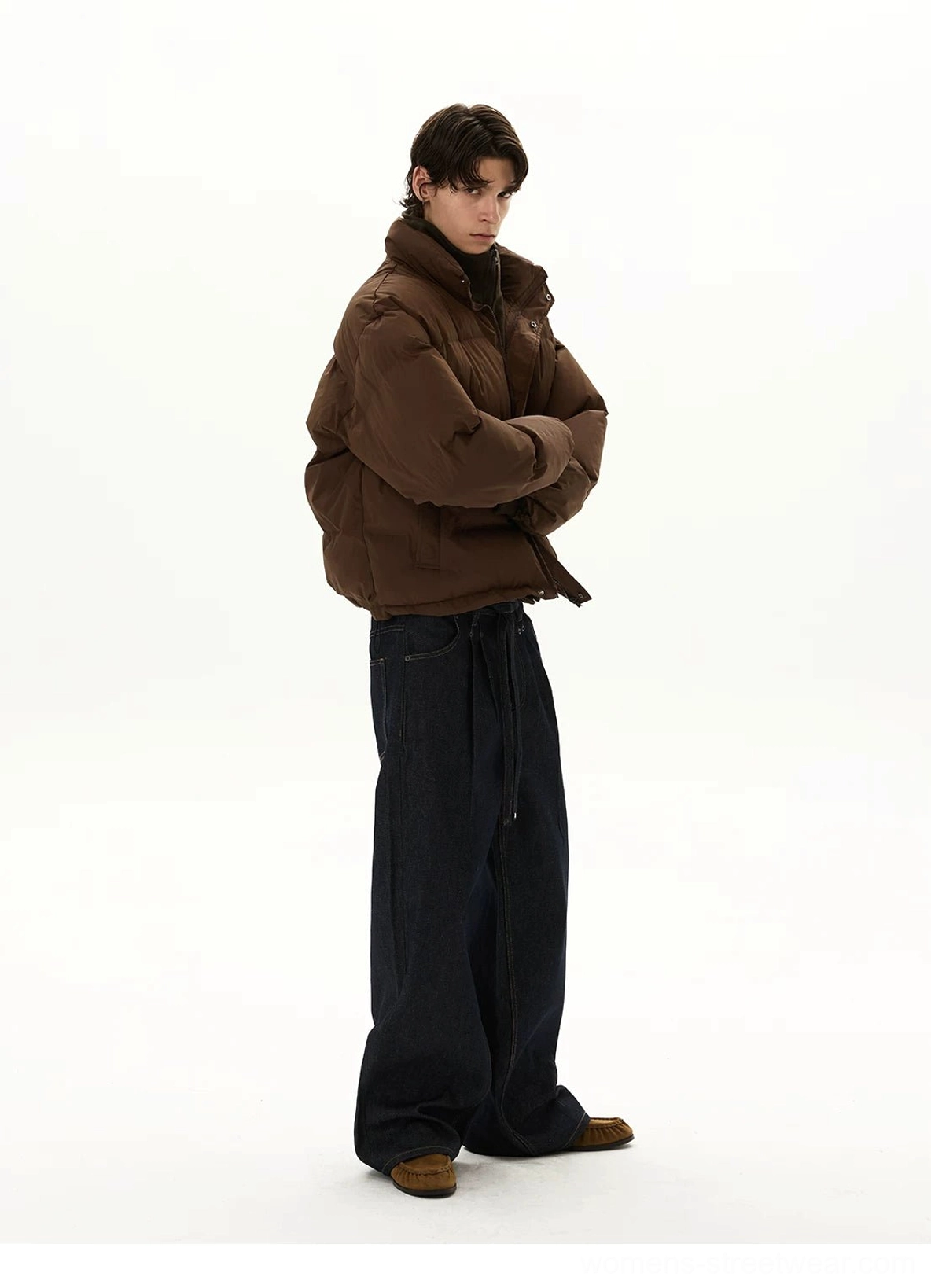 Side rear view of dark indigo wide-leg jeans styled with brown outerwear, stacked hems, relaxed balloon silhouette, and casual streetwear shoes