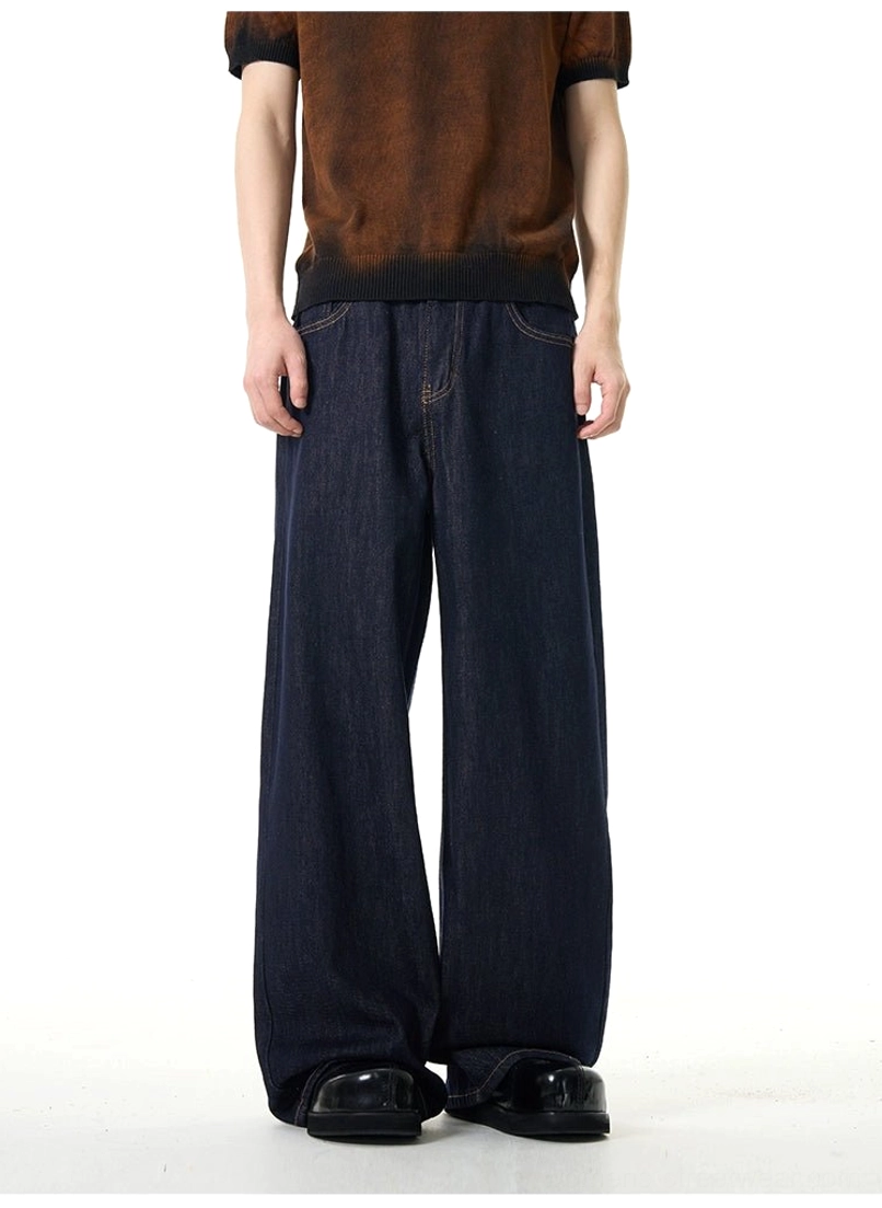Male model styling dark indigo wide-leg jeans with a brown gradient short-sleeve top and black leather shoes in a clean urban outfit