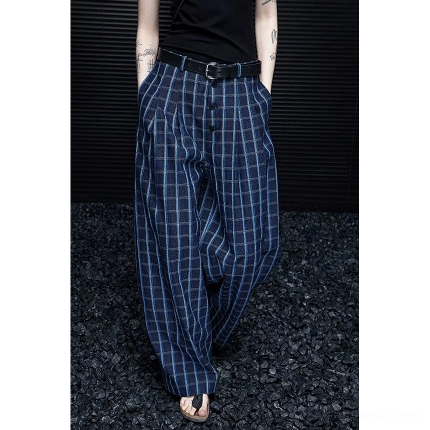Low-angle front detail of dark navy and light blue grid plaid wide-leg trousers with pleats, belt styling, and dramatic floor-length drape