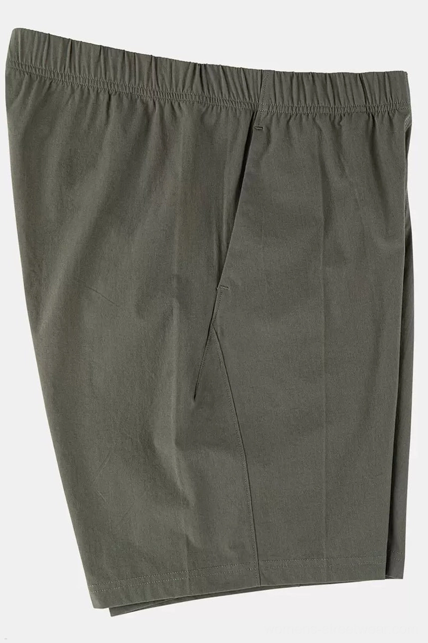 Three-quarter view of dark olive lightweight cotton tech shorts showing the elastic waistband, clean seams, and relaxed streetwear silhouette
