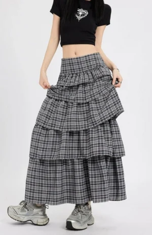 Front three quarter view of a black dark grey plaid tiered maxi skirt with high waist layered ruffles styled with a black cropped tee and silver chunky sneakers