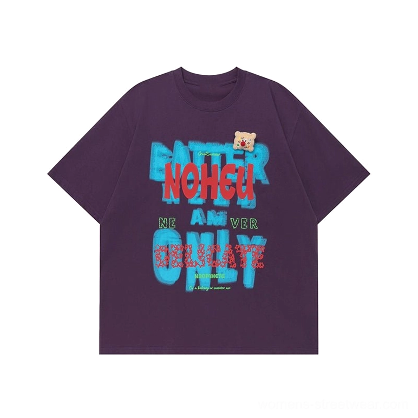 Dark purple oversized graphic T-shirt flat lay with colorful retro text print, crew neck, and teddy bear chest patch