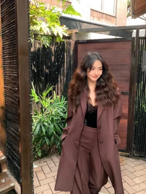 Dark reddish brown oversized mid-length blazer styled with wide-leg trousers in an outdoor courtyard, Seoul-inspired women’s tailored streetwear look