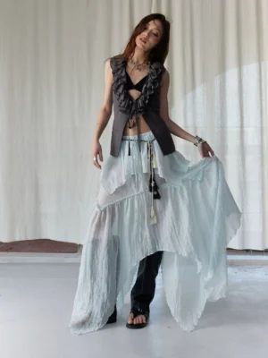 Full body front view of a woman wearing a dark ruffle vest with an asymmetric mint green layered skirt in an avant garde streetwear outfit