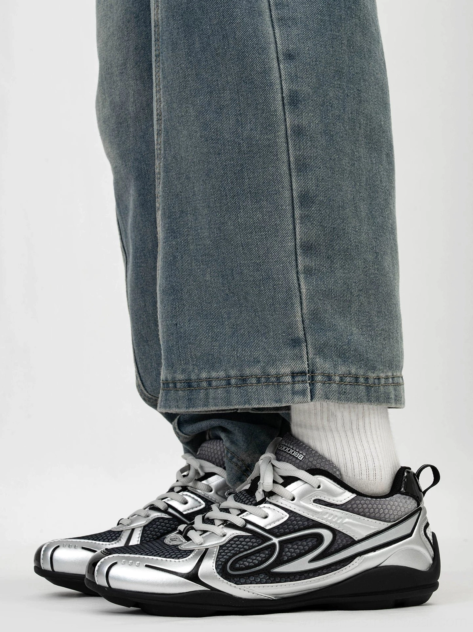Dark silver futuristic retro runner sneaker worn with loose blue jeans and white crew sock showing heel pull tab durable rubber outsole and low-top silhouette