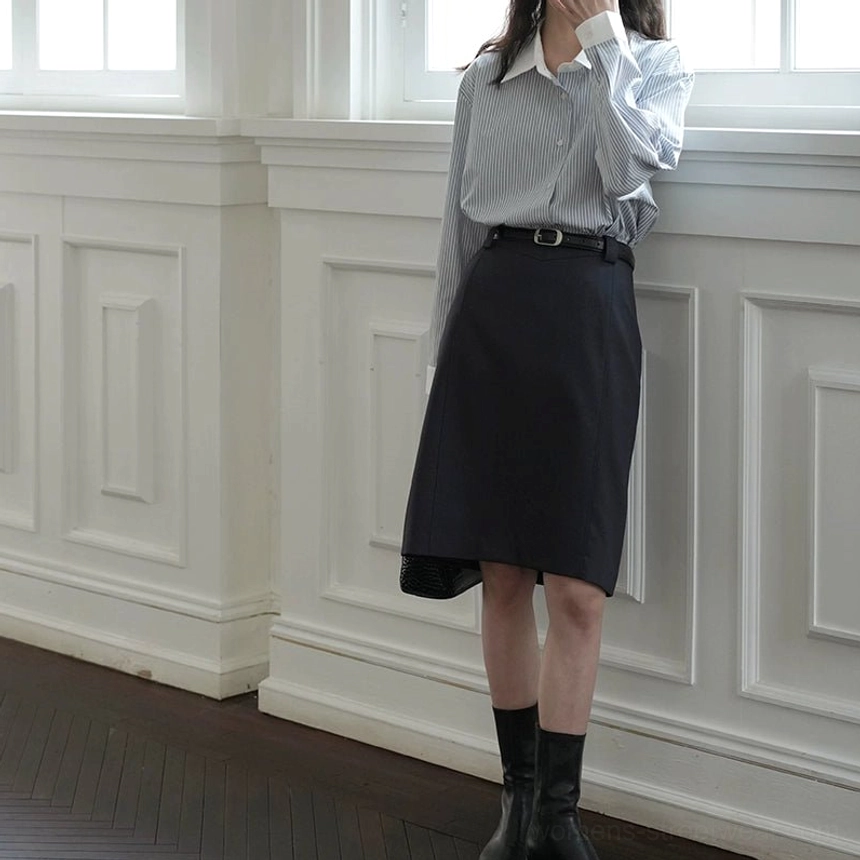 Dark tailored belted skirt shown from the back three-quarter view with a sleek black waist belt and refined urban streetwear aesthetic