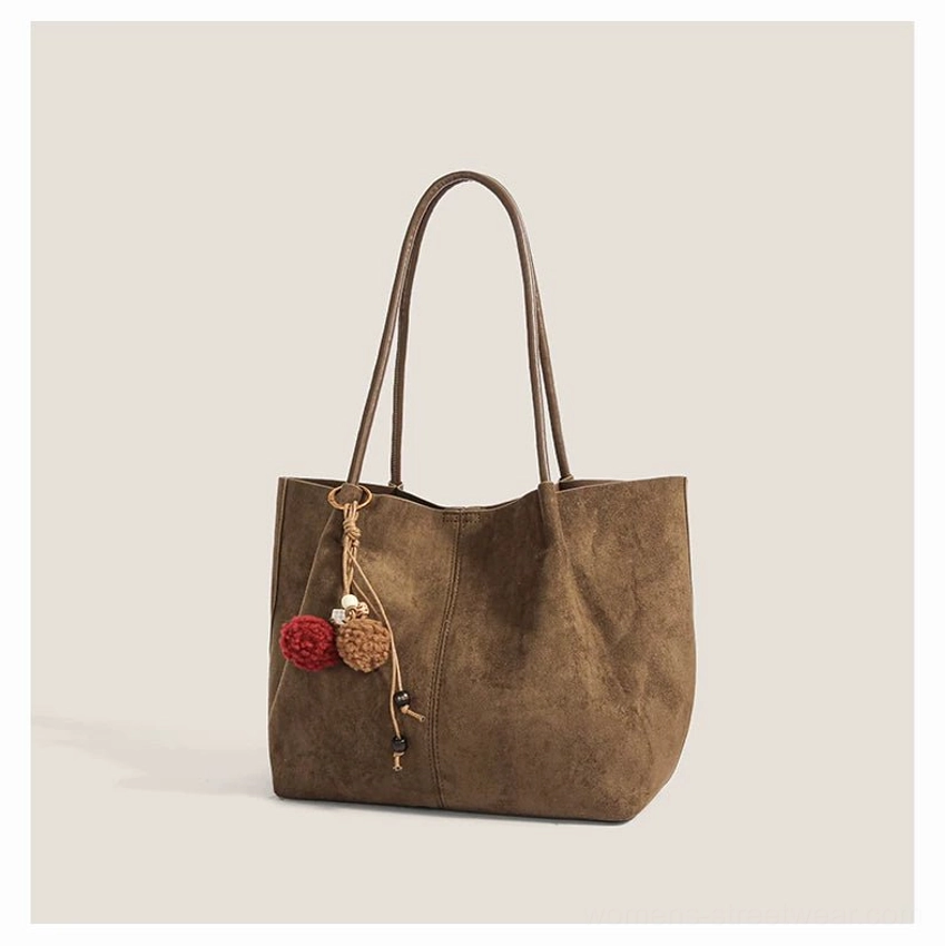 Dark taupe faux suede shoulder tote bag shown from the side with long straps and a decorative yarn pom pom tassel charm