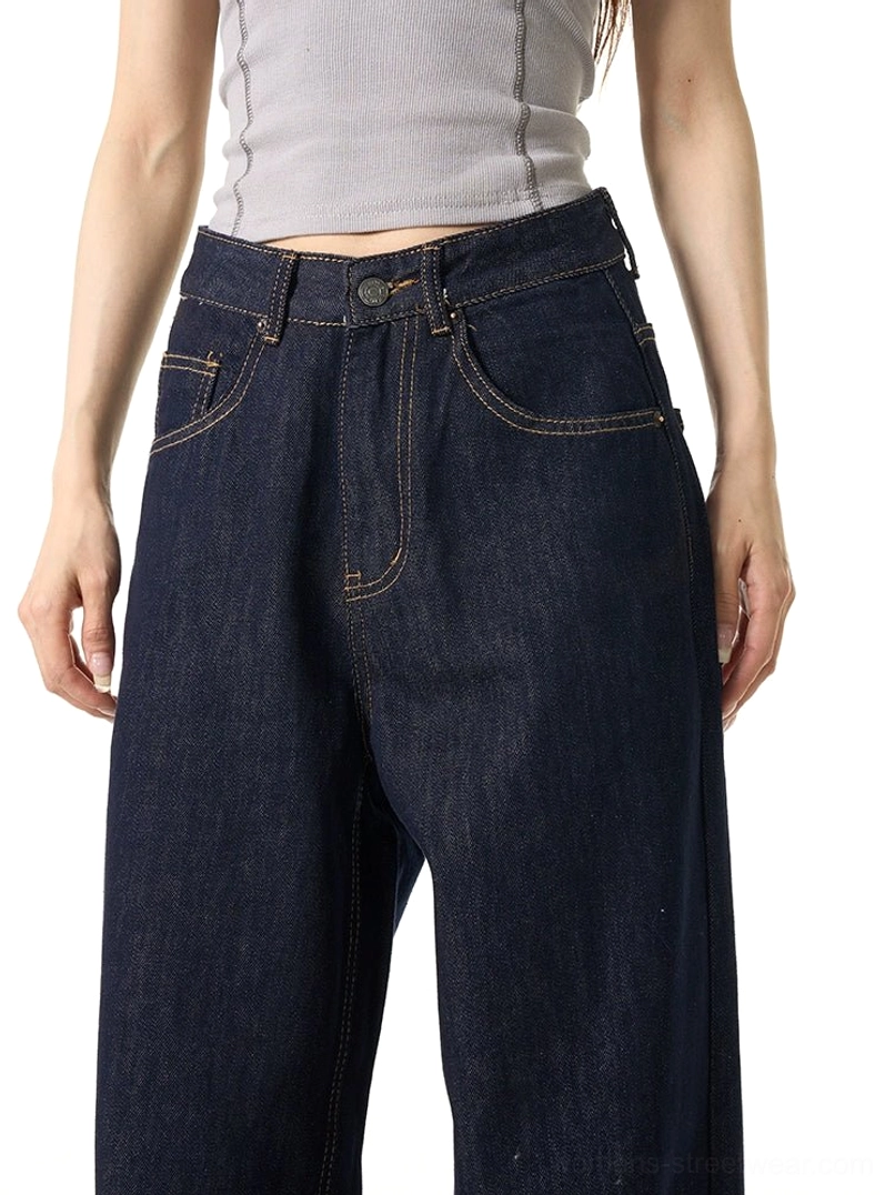 Close-up waist-down view of dark wash wide-leg jeans showing the button fly, classic pockets, contrast orange stitching, and cotton denim texture