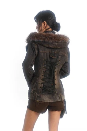 Back view of a dark washed denim military jacket showing the lace-up corset-style back, upper flap pocket, asymmetric hem, and fur-lined hood collar