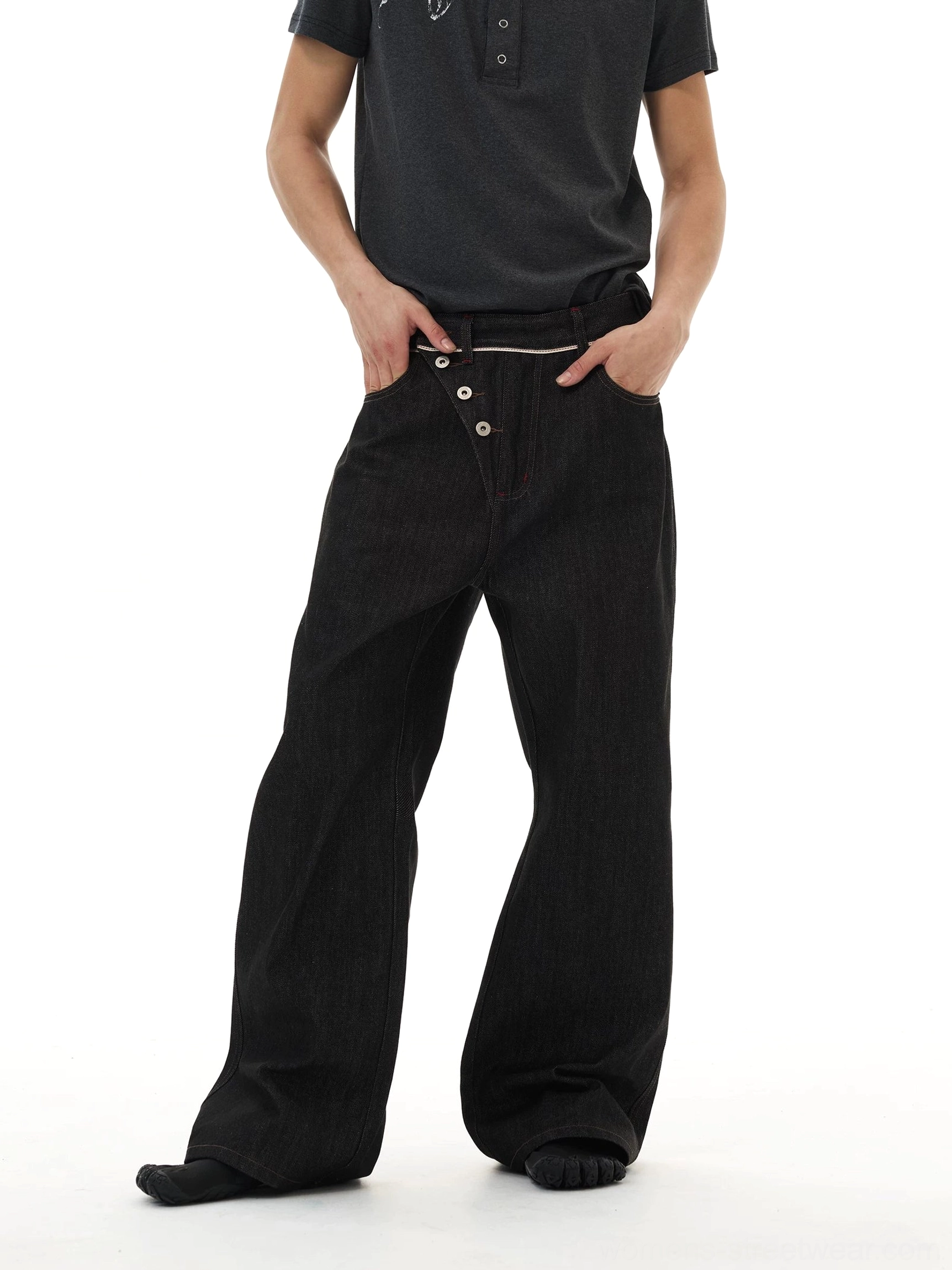 Three-quarter view of black deconstructed wide-leg denim jeans with asymmetric button waistband and contrast stitching