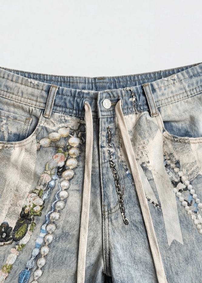 Close-up of decorated denim jorts button fly waistband drawstring pearl beads embroidery and faded blue wash