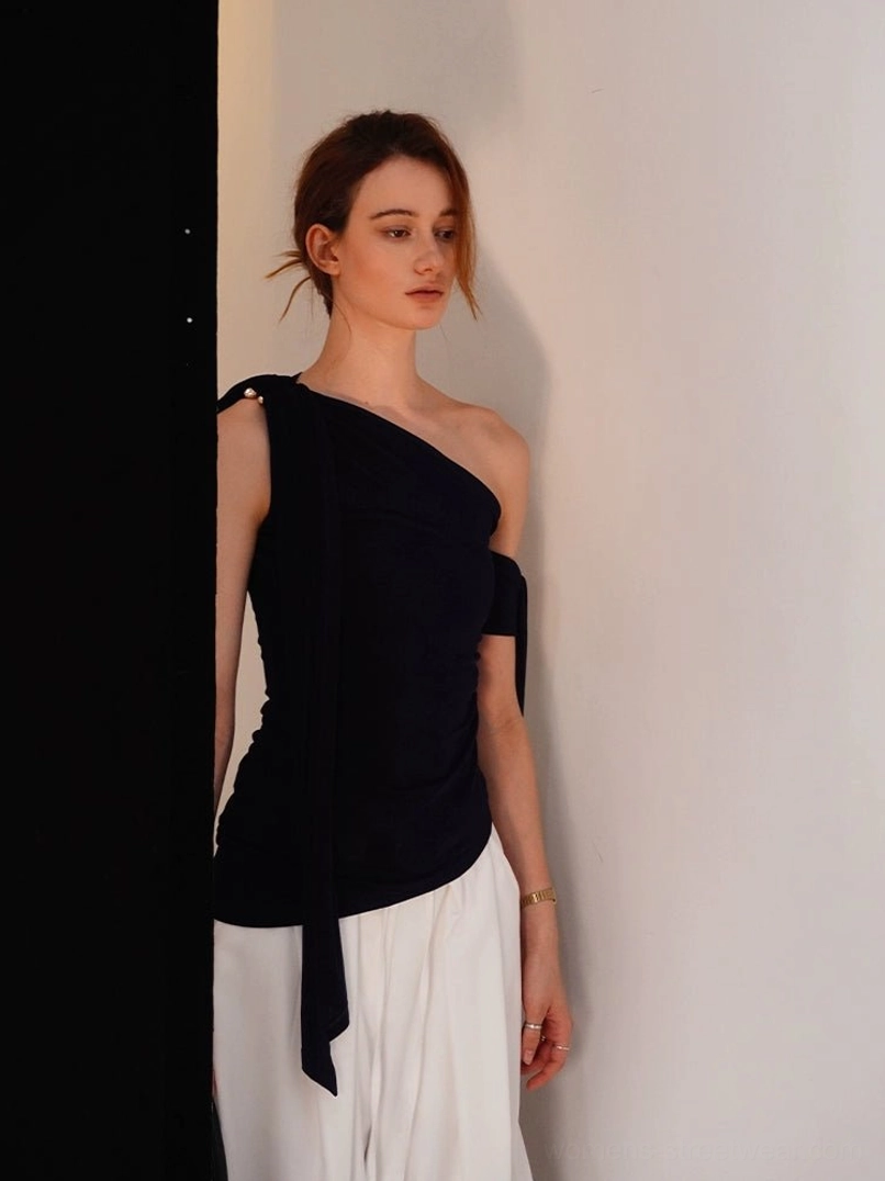 Close-up front view of a deep navy velvet asymmetric one-shoulder top with sculptural draped hem detail