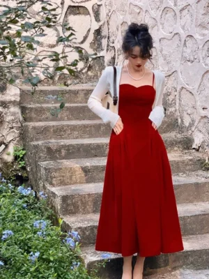 Full-length view of a deep red sweetheart camisole maxi dress with fitted bodice, pleated waist, flowing skirt, and practical side pockets on a stone stairway