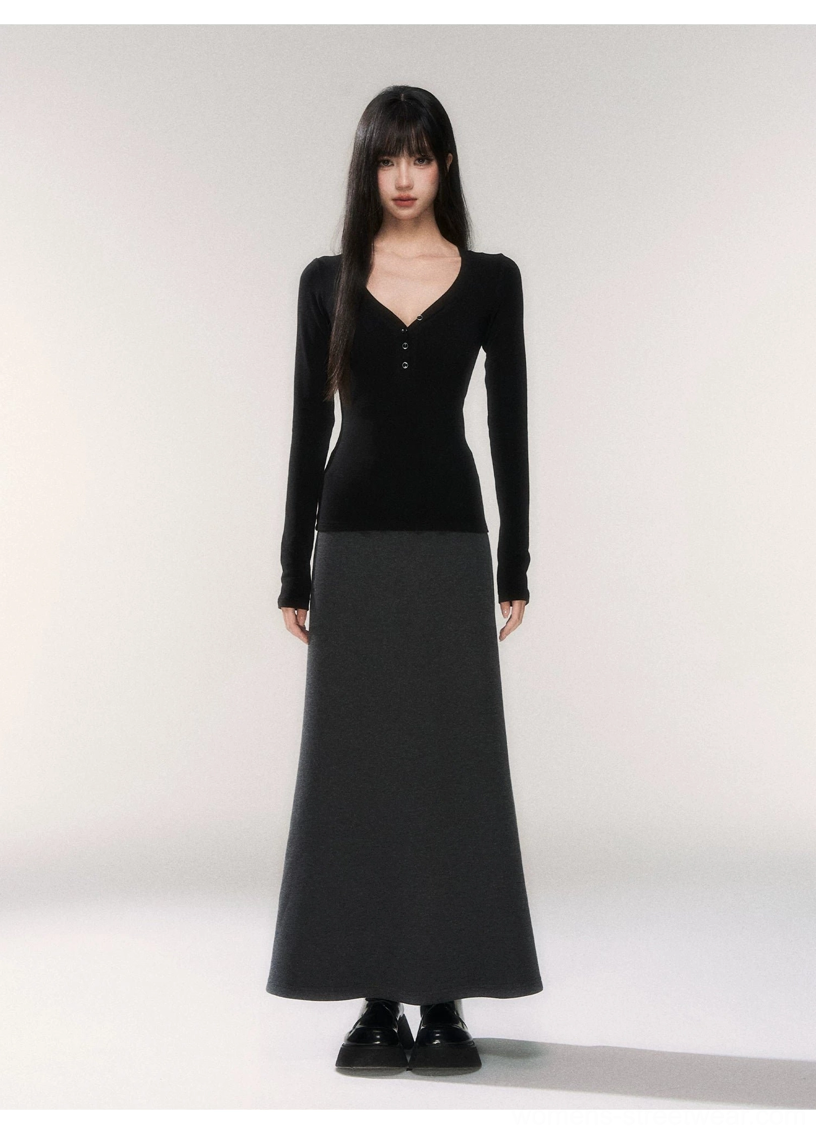 Black deep V-neck henley knit top with fitted long sleeves styled with a floor-length gray maxi skirt in a minimalist studio