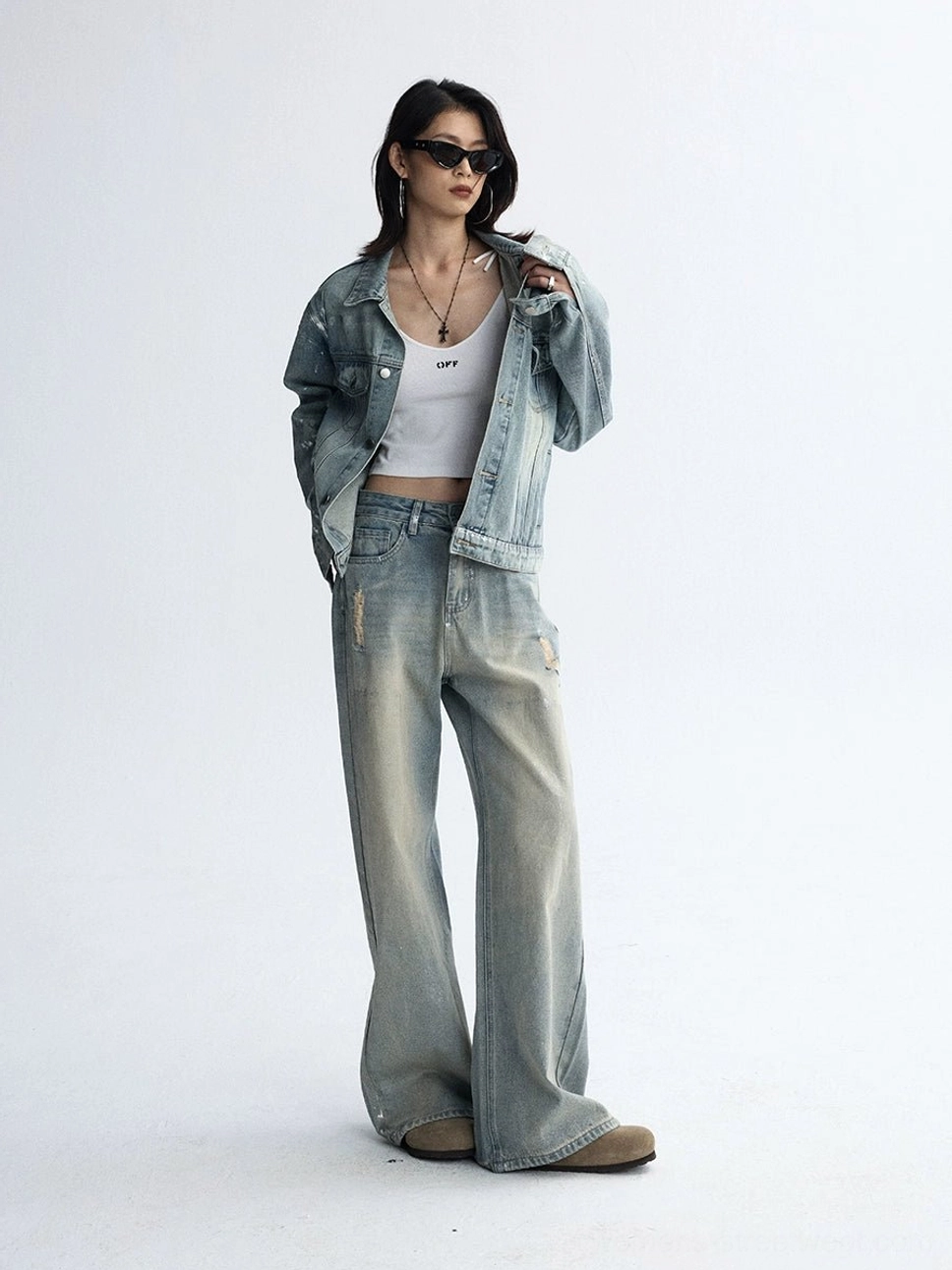Denim-on-denim Y2K outfit with distressed wide-leg jeans, cropped denim jacket, white crop top, layered necklaces, and sunglasses
