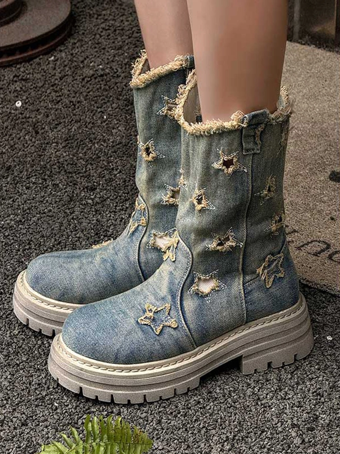 Front three-quarter view of denim platform boots worn with frayed cuffs, star distressed details, and thick light-colored sole
