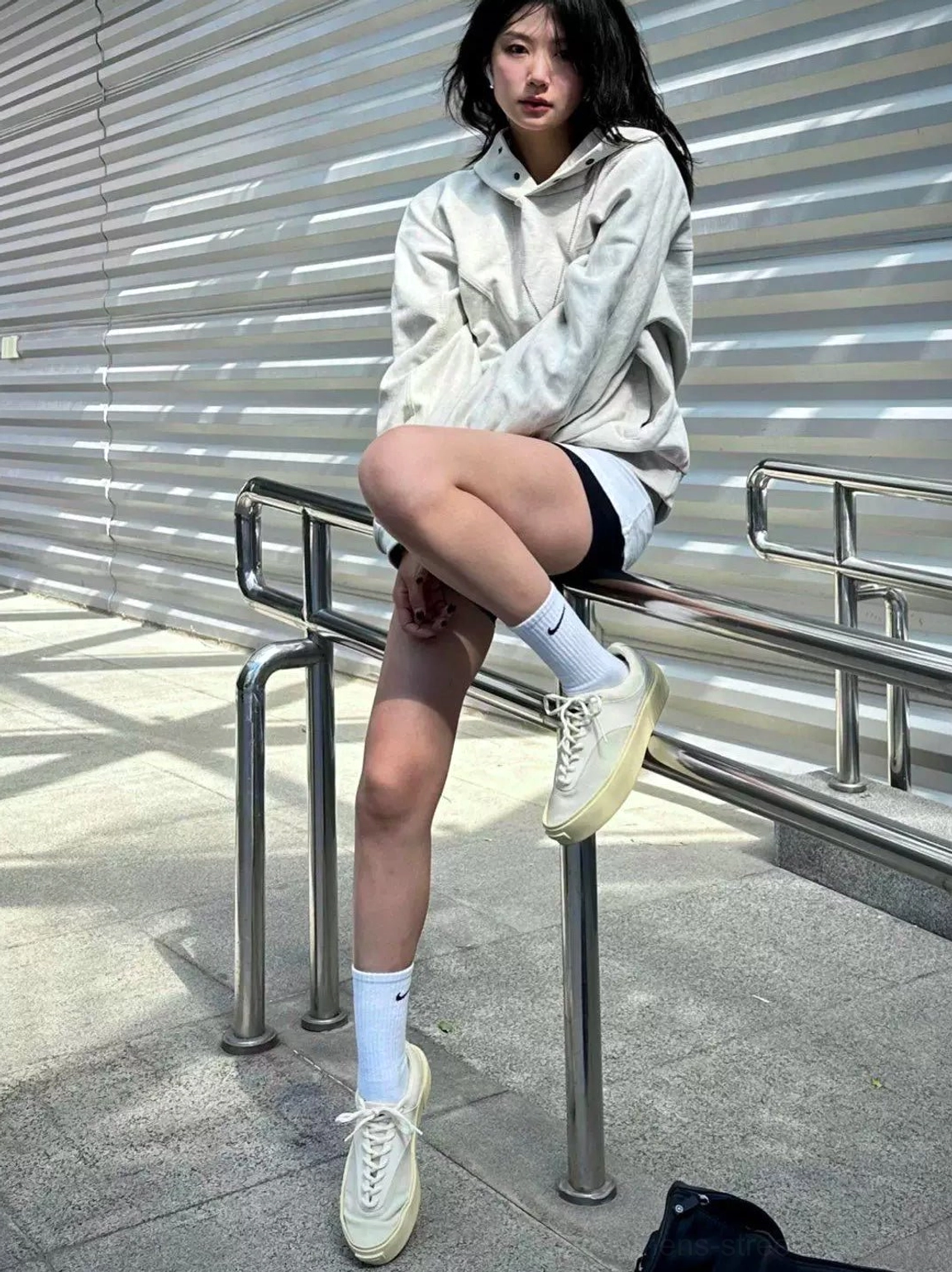 Female model wearing desert gray platform canvas sneakers with gray hoodie, shorts, and white crew socks in a modern outdoor streetwear setting